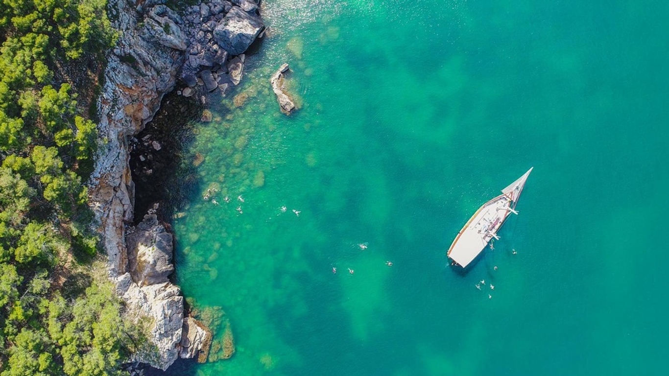 Birdseye view of a large sailing boat with swimmers in turqouise water